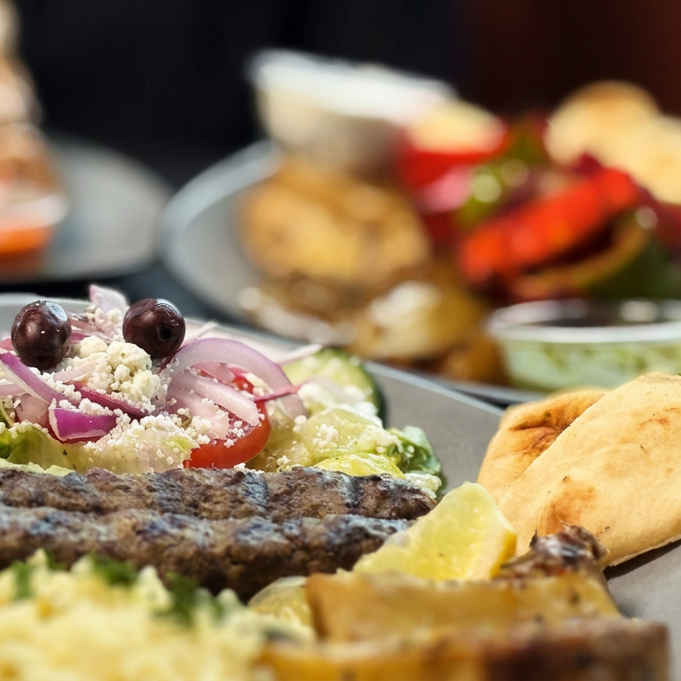 Mediterranean platter with grilled kebab, Greek salad, pita bread, hummus, and stuffed grape leaves on a table.