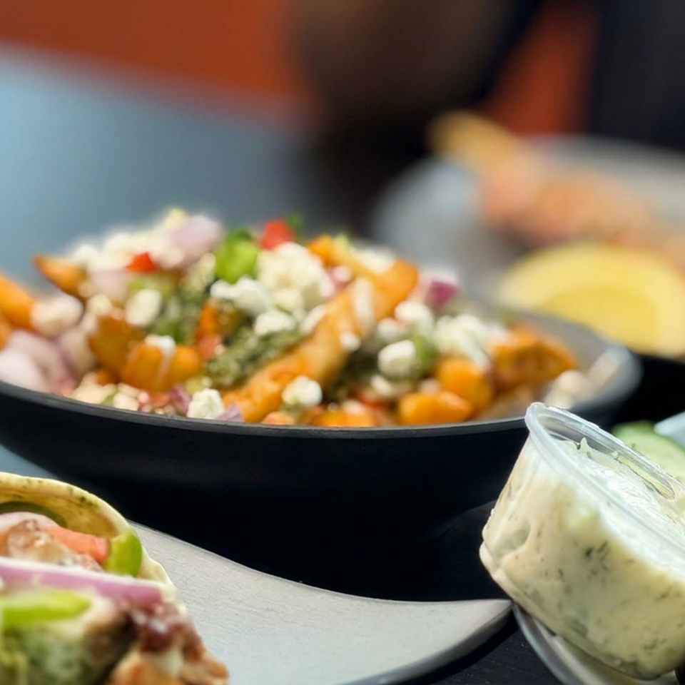 Assorted Mediterranean dishes with roasted vegetables, salad, pita wraps, falafel, and creamy dip arranged on a restaurant table.